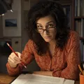 An editor looking over her glasses with a red pencil poised above a manuscript page